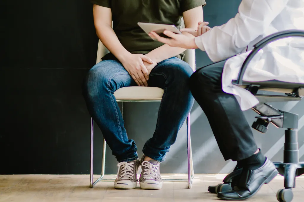 A man holds his groin to indicate BPH-related issues while in a doctor’s office.