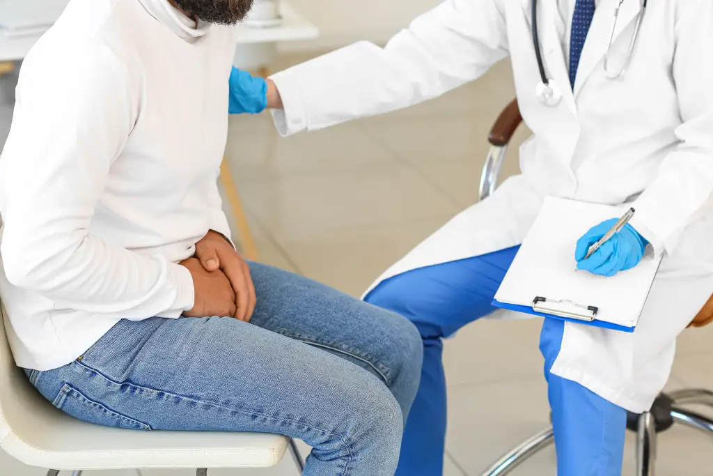 A physician consults with a patient holding his groin, demonstrating discomfort related to a prostate issue.