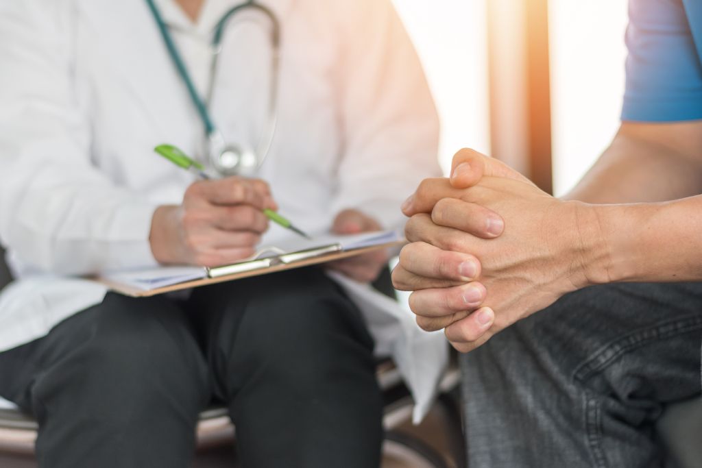 A physician takes notes while consulting with a patient.